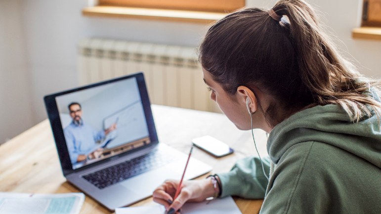Student taking handwritten notes while watching an AES instructor on her laptop